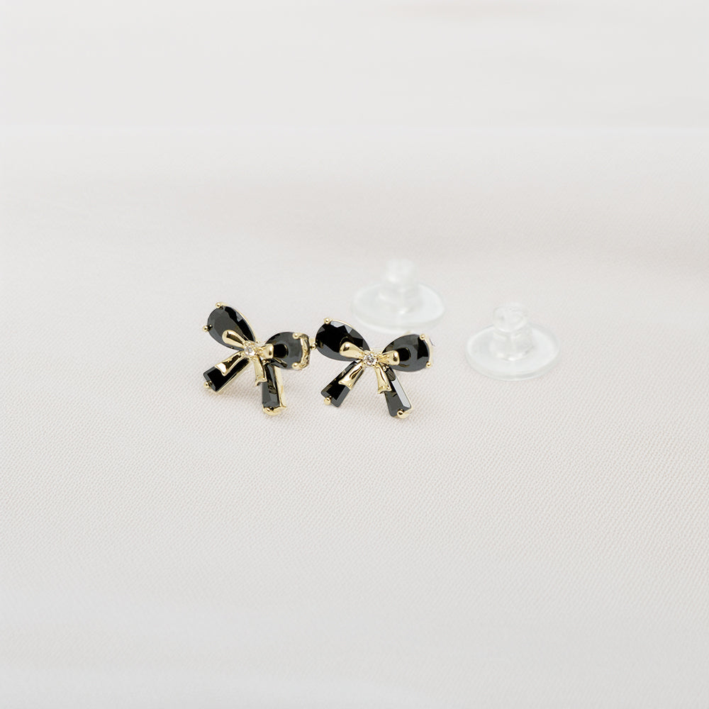 Elegant black and gold bow earrings with clear backings on white fabric