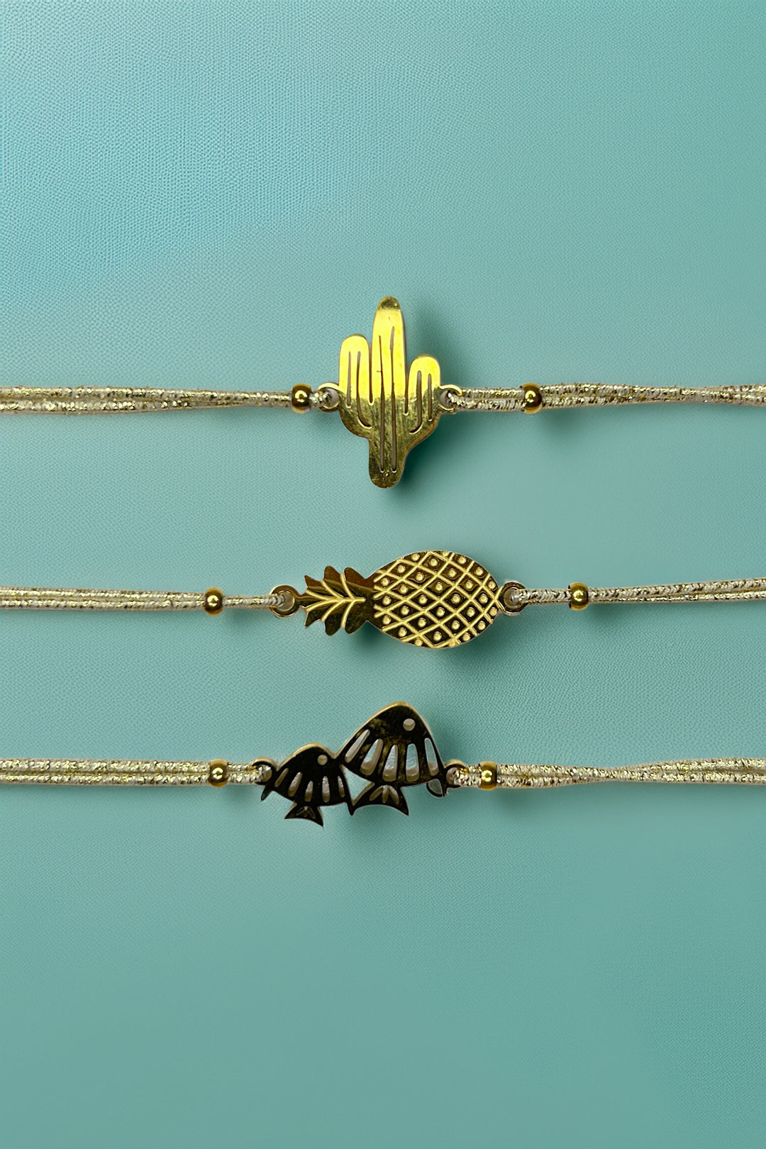 Gold charm bracelets with cactus, pineapple, and fish designs on a teal background
