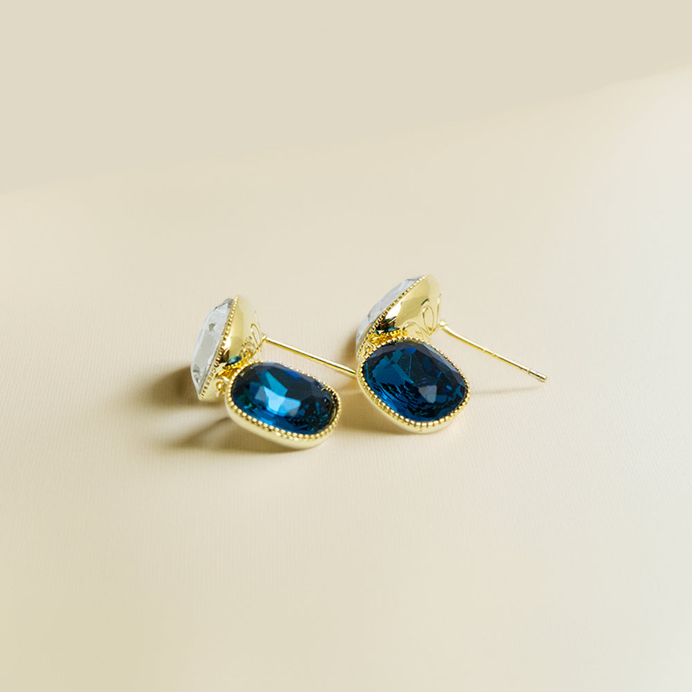 Elegant blue crystal and gold frame earrings on a beige background
