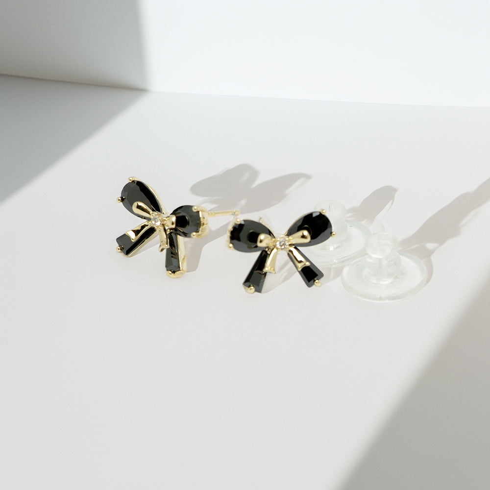 Black bow earrings casting shadows on a white background