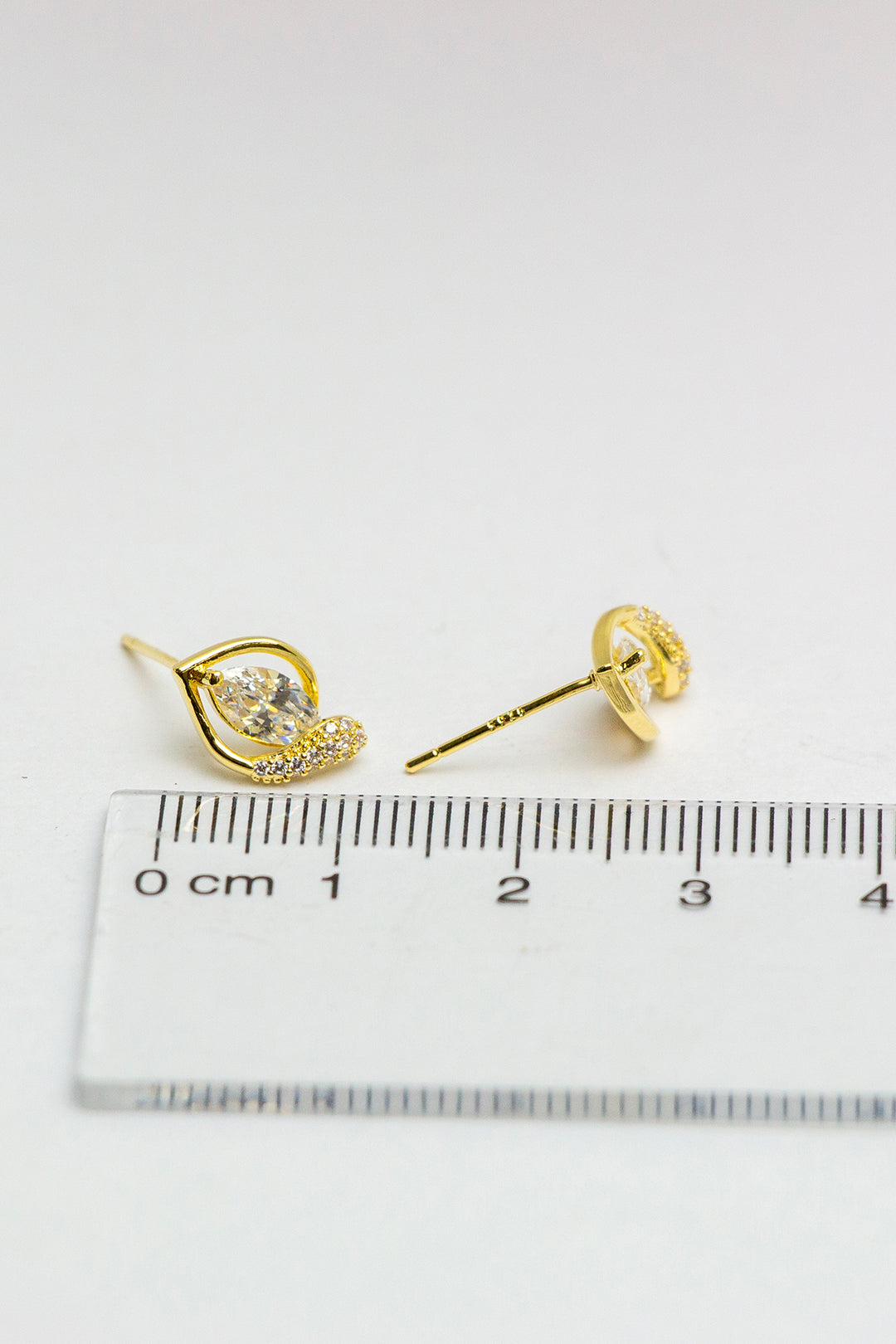Gold stud earrings, detailed close-up with ruler