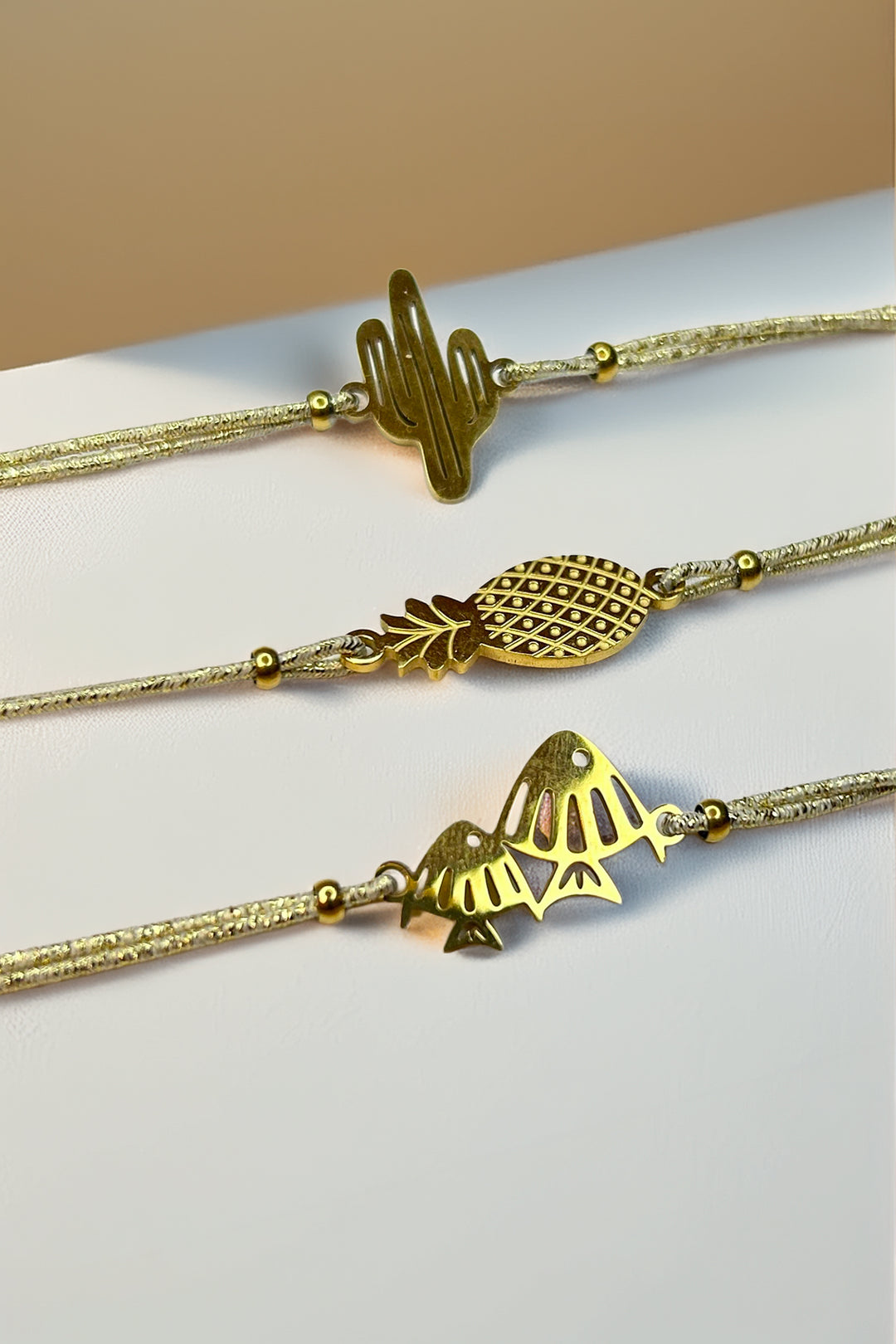 Side view of gold charm bracelets with a cactus, pineapple, and fish on a white surface