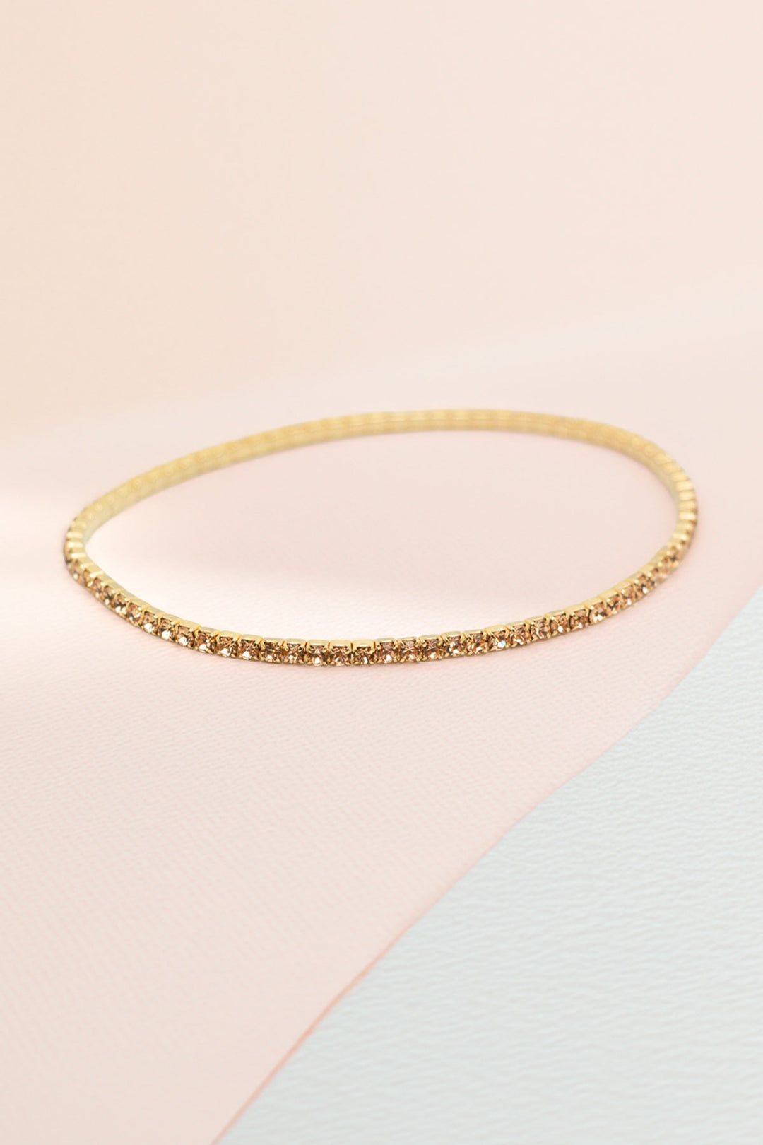 Single gold-tone rhinestone bangle on a soft pink background