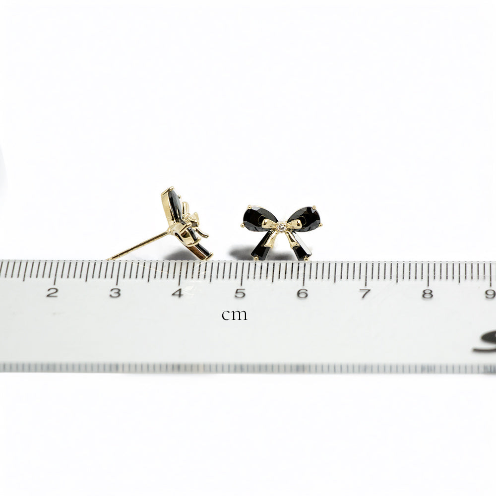 Black bow earrings next to a ruler indicating size