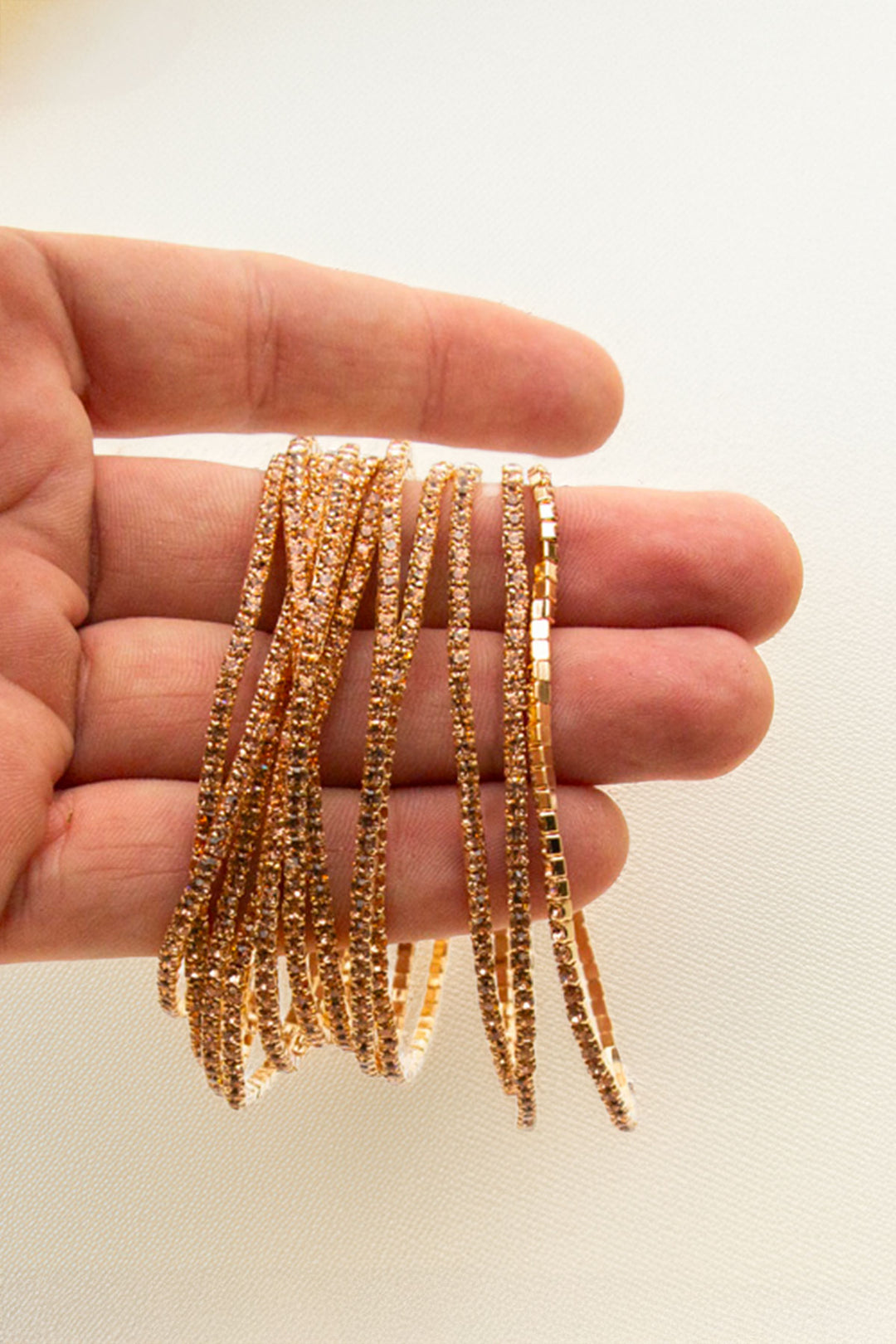 Hand holding multiple gold-tone rhinestone bangles