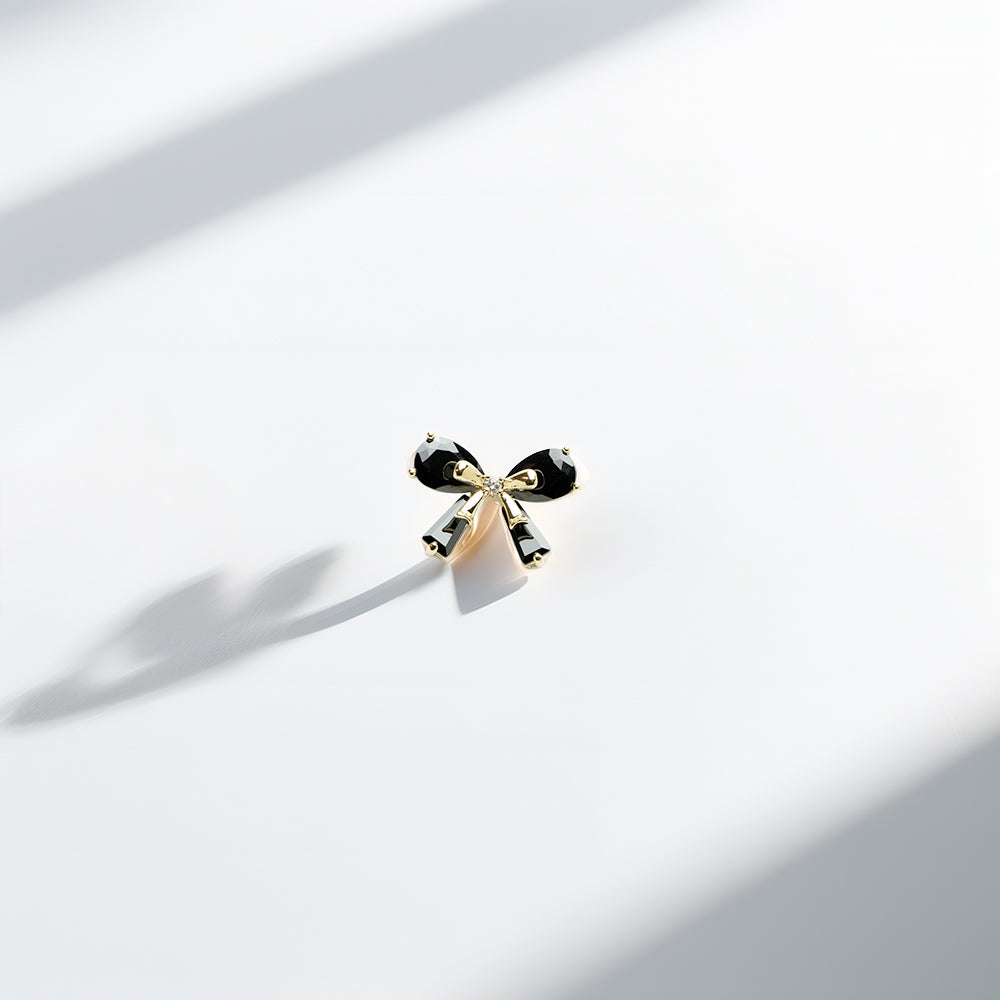 Single black bow earring on white with soft shadows