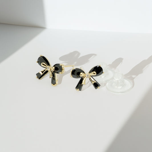 Black bow earrings casting shadows on a white background
