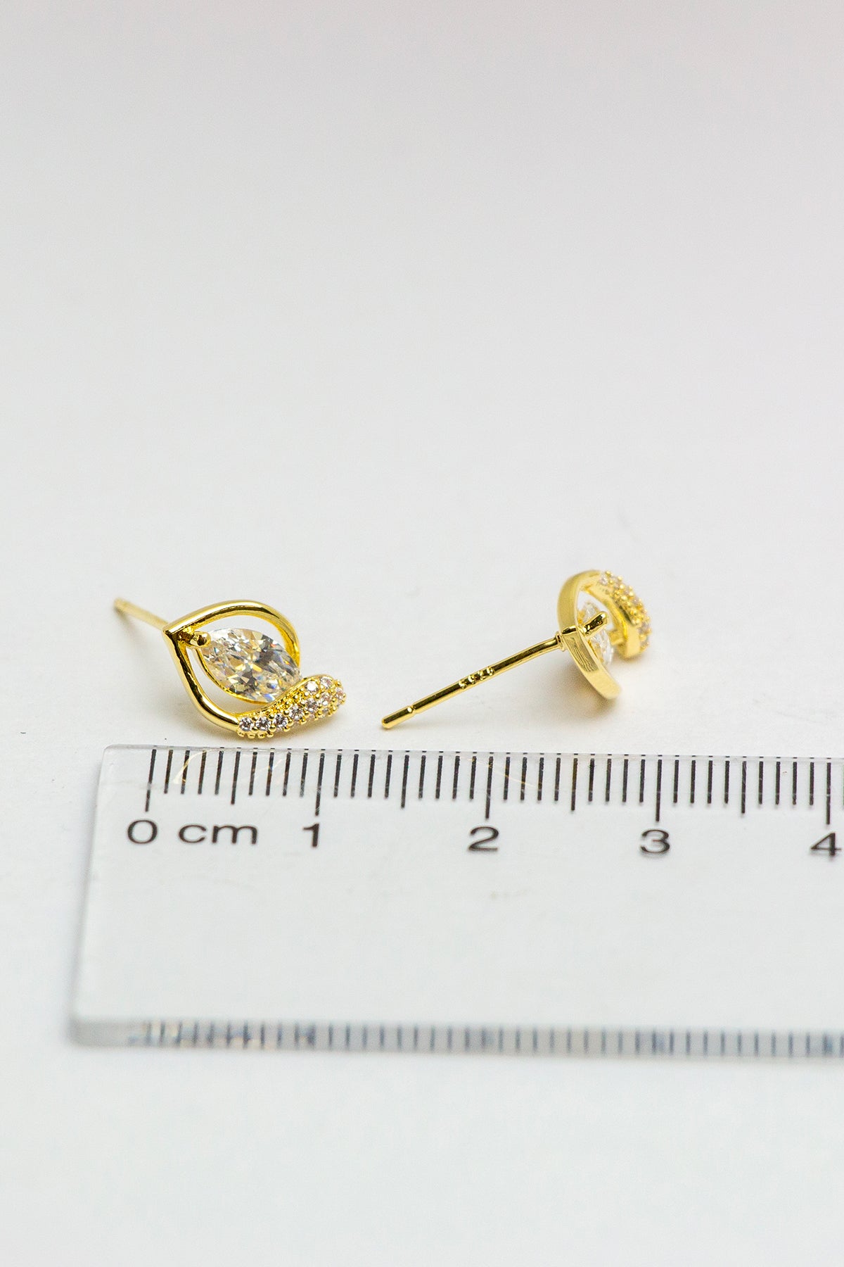 Gold stud earrings, detailed close-up with ruler