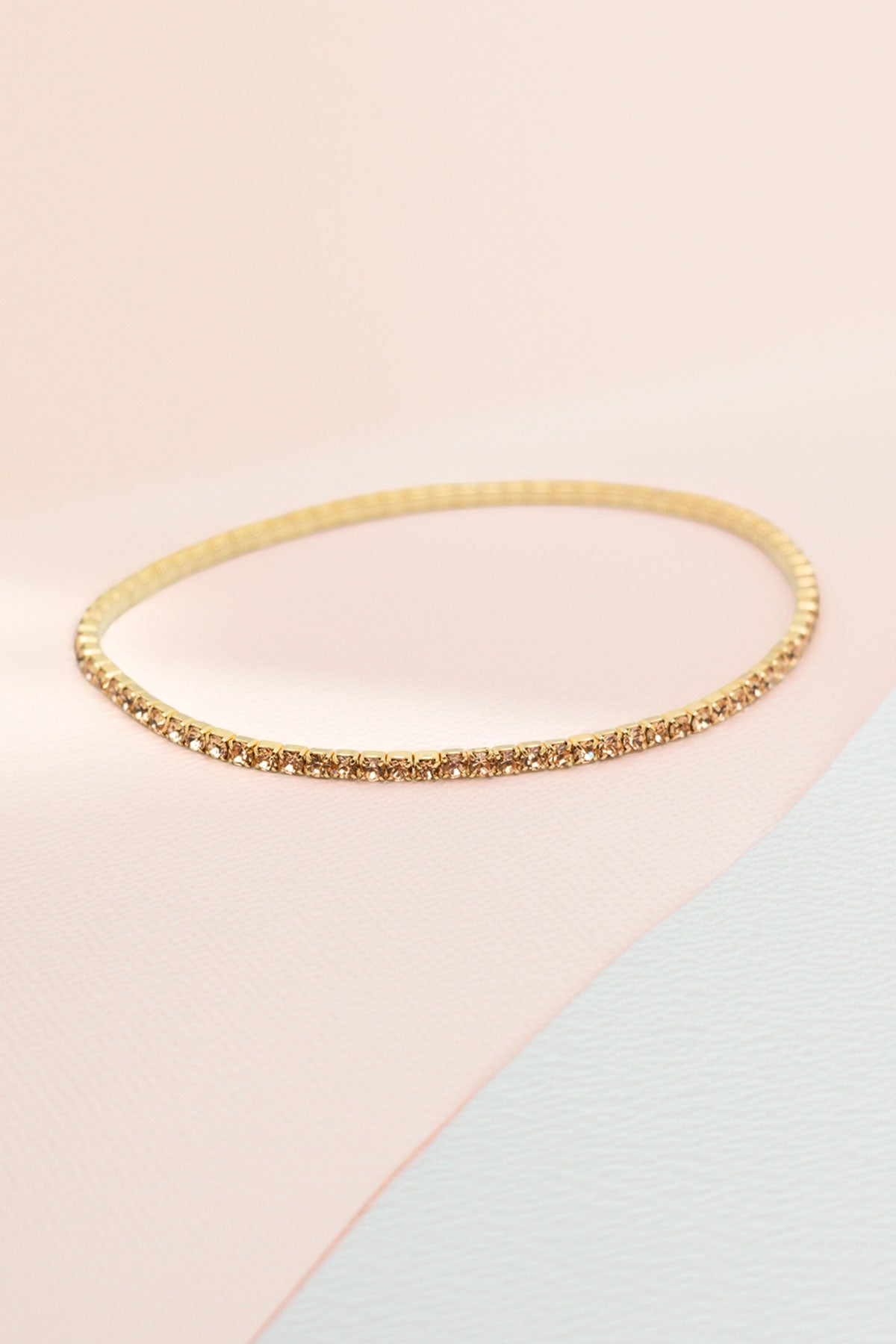 Single gold-tone rhinestone bangle on a soft pink background