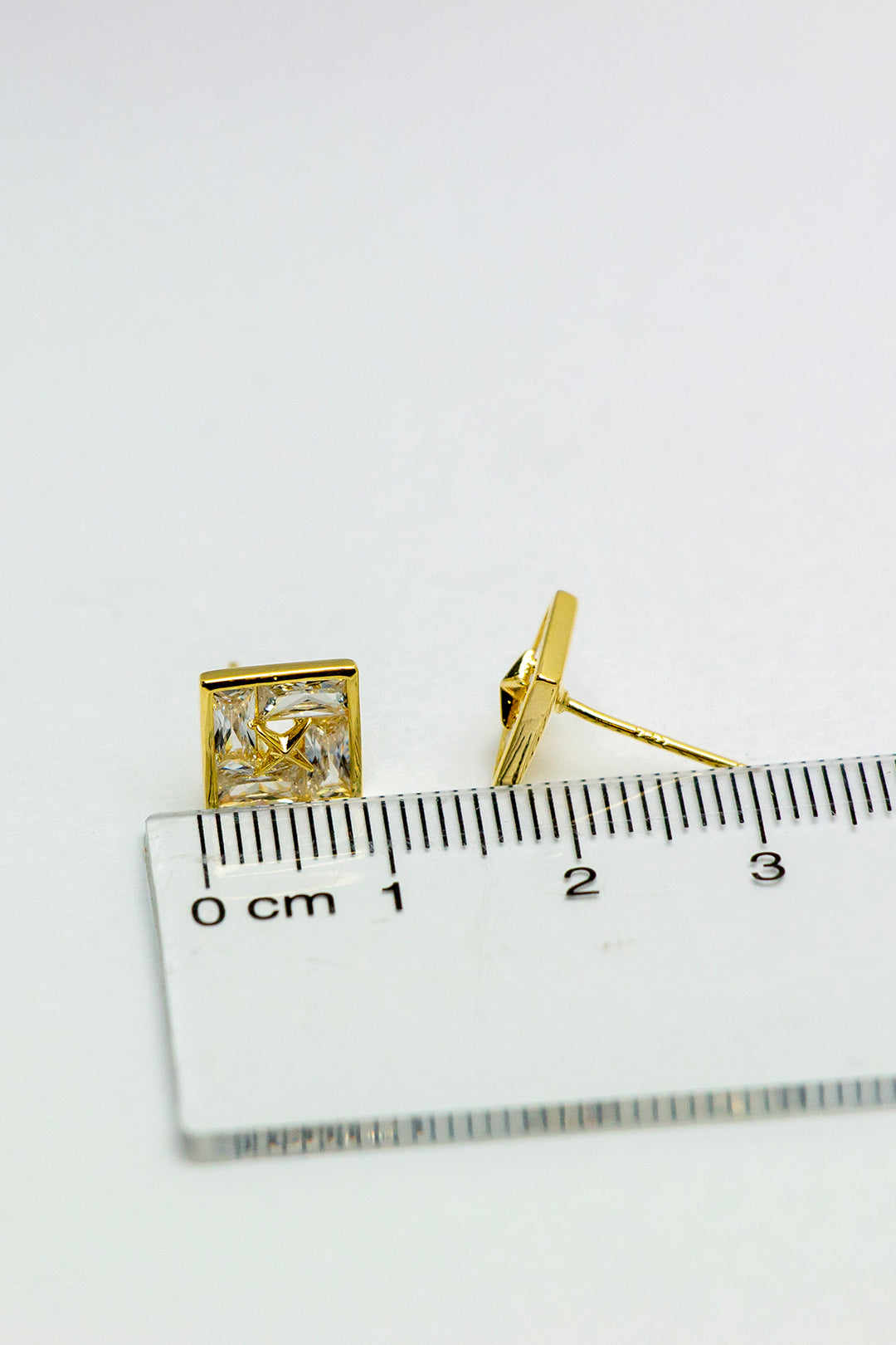 Gold-tone stud earrings with ruler for scale