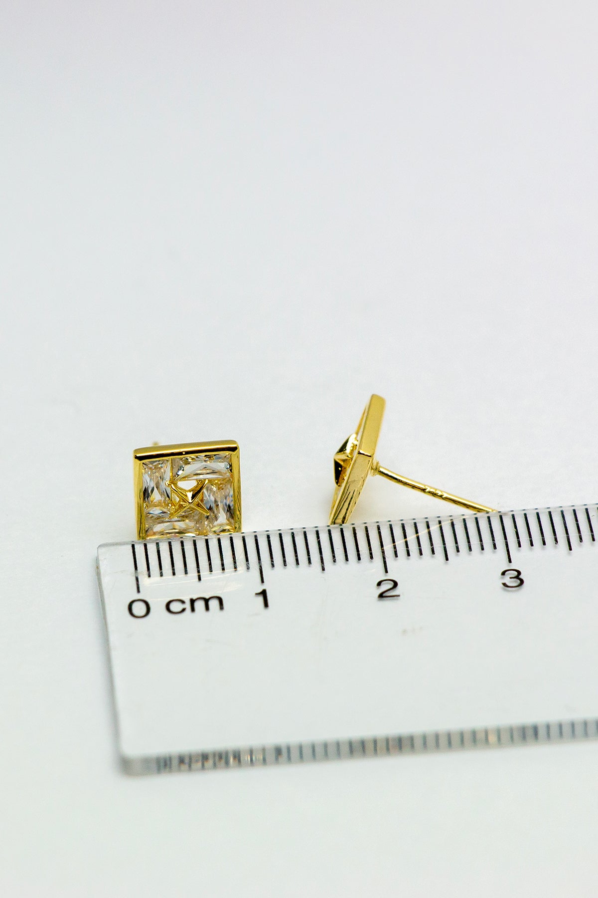 Gold-tone stud earrings with ruler for scale